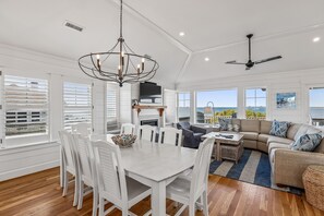 A spacious living area with a dining table, seating, a fireplace, and a view of the outdoors. - Knot for Sail -- Newer Soundfront Home with Hot Tub and Firepit (Duck)