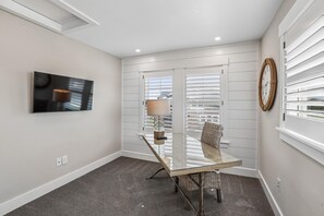 Une chambre moderne avec une table en verre, un téléviseur fixé au mur et une fenêtre avec des stores.