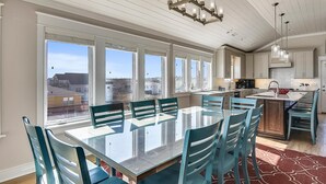 Un comedor amplio con una mesa grande y sillas, una cocina con electrodomésticos modernos, y ventanas grandes con vistas a la ciudad.