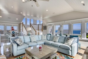 A spacious living room with a large sectional sofa, a wooden coffee table, and a view of the ocean through large windows. - Fantasea -- Spectacular Semi OF Home in Kitty Hawk w/Elevator, Pool and Ocean Views (Kitty Hawk)