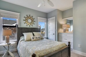 A bedroom with a bed, a nightstand, a dresser, a mirror, a ceiling fan, and a wall decoration. - Fantasea -- Spectacular Semi OF Home in Kitty Hawk w/Elevator, Pool and Ocean Views (Kitty Hawk)