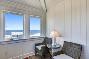 A room with two wicker chairs, a small table with a lamp, and a view of the ocean through large windows.