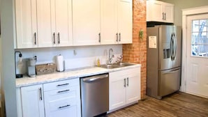 A kitchen with white cabinets, a stainless steel dishwasher, and a refrigerator. - The Dragonfly- A Historic Gem with Hot Tub (Franklin)