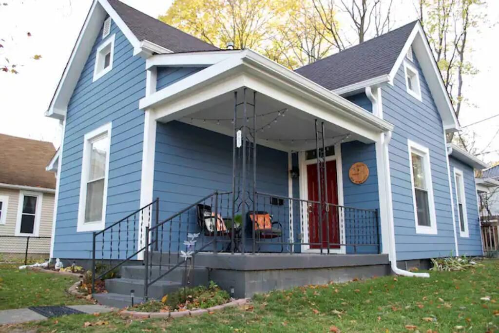 A two-story house with a front porch, a red door, and a small front yard.