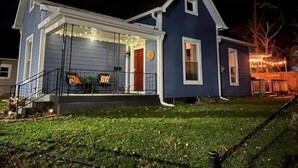 A two-story house with a covered front porch, a visible garage door, and a small attached shed. - The Dragonfly- A Historic Gem with Hot Tub (Franklin)