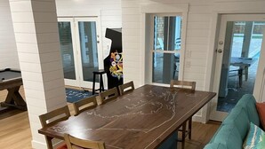 A dining area with a wooden table and chairs, a teal sofa with orange cushions, and a pool table in the background. - Austin -- New Construction Oceanfront 11BR with Elevator, Fire Pit, Pool, Fitness Room and More! (Corolla)