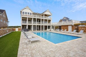 A two-story building with a swimming pool, outdoor seating, and a well-maintained lawn.