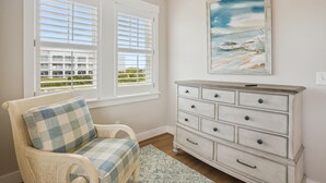 A room with a view of a building through a window, a chair with a checkered cushion, and a white dresser with multiple drawers. - Austin -- New Construction Oceanfront 11BR with Elevator, Fire Pit, Pool, Fitness Room and More! (Corolla)