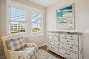 A room with a view of a building through a window, a chair with a checkered cushion, and a white dresser with multiple drawers. - Austin -- New Construction Oceanfront 11BR with Elevator, Fire Pit, Pool, Fitness Room and More! (Corolla)