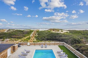 Una piscina en la azotea con sillones de descanso, una terraza de madera y vistas a la playa y el océano.
