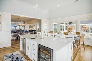A spacious kitchen with a large island, white cabinetry, and a view to the dining area. - Basnight -- Beautiful New Construction Oceanfront Home with Elevator, Theater, Gameroom and Ocean Views! (Corolla)