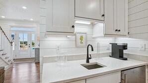 A modern kitchen with white cabinetry, a black faucet, and a coffee maker. - Newbern - New Cons. Semi Oceanfront in Corolla with Fire Pit, Elevator, Hot Tub and More! (Corolla)