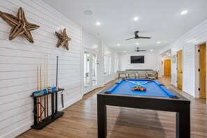 A pool table with billiard balls, a pool cue rack, and cue sticks against a white paneled wall. - Newbern - New Cons. Semi Oceanfront in Corolla with Fire Pit, Elevator, Hot Tub and More! (Corolla)