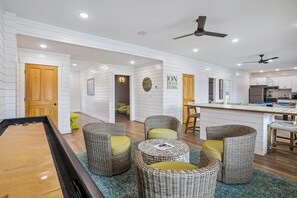 A spacious living area with a pool table, wicker furniture, and a kitchen area with modern appliances. - Newbern - New Cons. Semi Oceanfront in Corolla with Fire Pit, Elevator, Hot Tub and More! (Corolla)