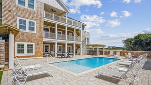 A two-story building with a swimming pool, outdoor seating, and a covered patio area. - Newbern - New Cons. Semi Oceanfront in Corolla with Fire Pit, Elevator, Hot Tub and More! (Corolla)
