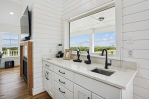 A modern kitchen with white cabinetry, a large window, and a view of the outdoors. - Newbern - New Cons. Semi Oceanfront in Corolla with Fire Pit, Elevator, Hot Tub and More! (Corolla)