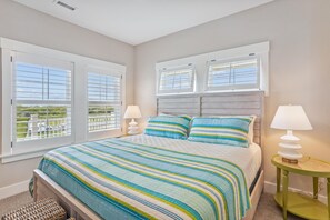 A bedroom with a large bed, two bedside lamps, and a view of greenery through the windows. - Newbern - New Cons. Semi Oceanfront in Corolla with Fire Pit, Elevator, Hot Tub and More! (Corolla)