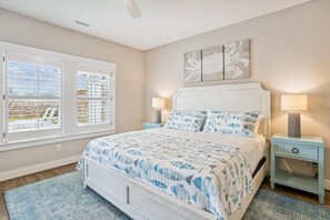 A bedroom with a bed, two bedside tables, a window with blinds, and a ceiling fan. - Newbern - New Cons. Semi Oceanfront in Corolla with Fire Pit, Elevator, Hot Tub and More! (Corolla)