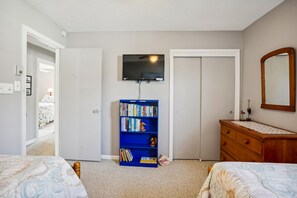 Un dormitorio con dos camas, una estantería, un aparador, un televisor y una puerta.