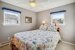 A bedroom with a bed, two windows with curtains, a ceiling fan, a wall-mounted lamp, and a framed picture. - New Listing!  Reel-M-Inn -- Classic Nags Head Beach house just 2 blocks to Ocean (Nags Head)