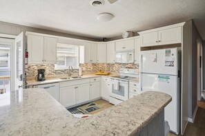 Una cocina con armarios blancos, microondas, refrigerador y cafetera.