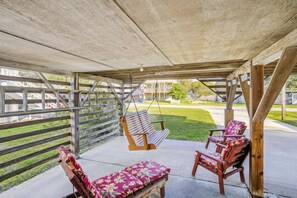 A covered outdoor seating area with a swing, two chairs with floral cushions, and a wooden pergola structure.