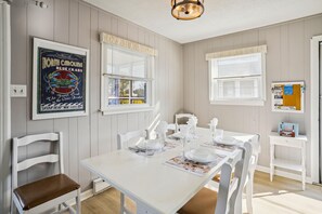 Comedor con mesa blanca dispuesta para cuatro, sillas blancas y un tablón de anuncios con varios avisos.