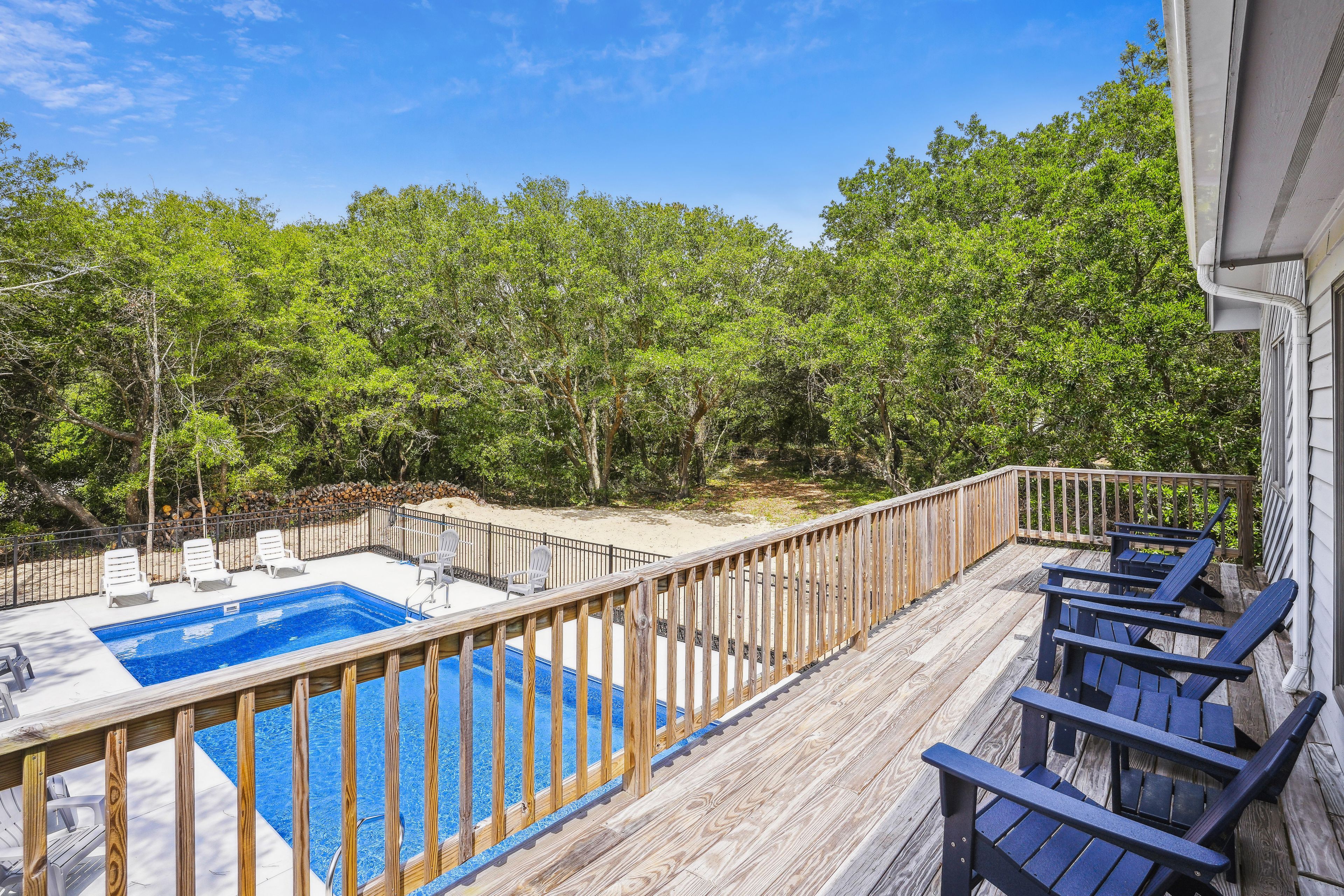 A wooden deck with a pool and lounge chairs, surrounded by trees.