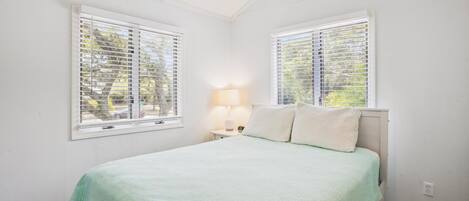A bedroom with a bed, two windows, a nightstand, and a lamp.