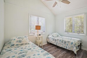 Une chambre avec deux lits simples, une table de chevet avec une lampe et un ventilateur de plafond.