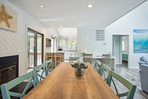 A spacious dining area with a wooden table and chairs, a kitchen in the background, and a view of the outdoors.