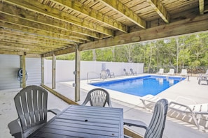 Un área de piscina al aire libre con una pérgola de madera, sillones de descanso y una mesa.