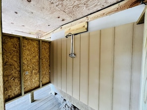 A room with wooden walls and a sloped ceiling, a shower area with a metal showerhead, and a wooden floor.