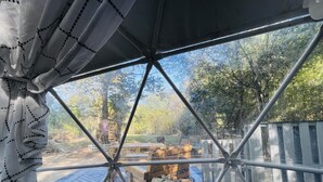A geodesic dome structure with a view of an outdoor area featuring a wooden deck, a fire pit, and a rustic wooden table.