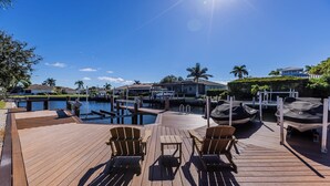 A wooden deck with lounge chairs, a small pool, and a marina with boats.