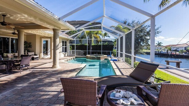 A covered outdoor area with a pool, lounge chairs, and a view of a body of water.