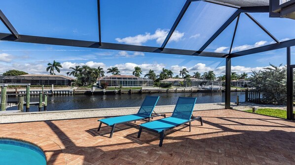 Un espacio al aire libre cubierto con dos sillones azules, una piscina y vistas a un puerto deportivo con barcos y palmeras.