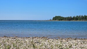 Kivikkoinen rantaviiva, kirkas sininen vesi ja kauempana näkyvä metsäinen saari.