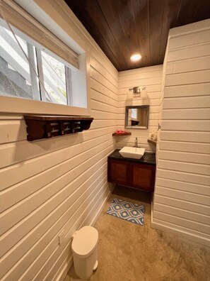 Bathroom features a toilet, sink, and mirror, with a window and shelf.