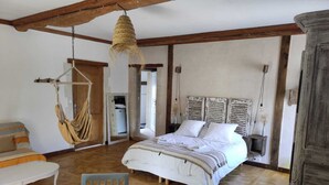 A bedroom with a bed, a hanging chair, a table, and a chair. - Chambre D'hôte à La Cour Souveraine Près des Plages du Débarquement et de Bayeux (Mosles)