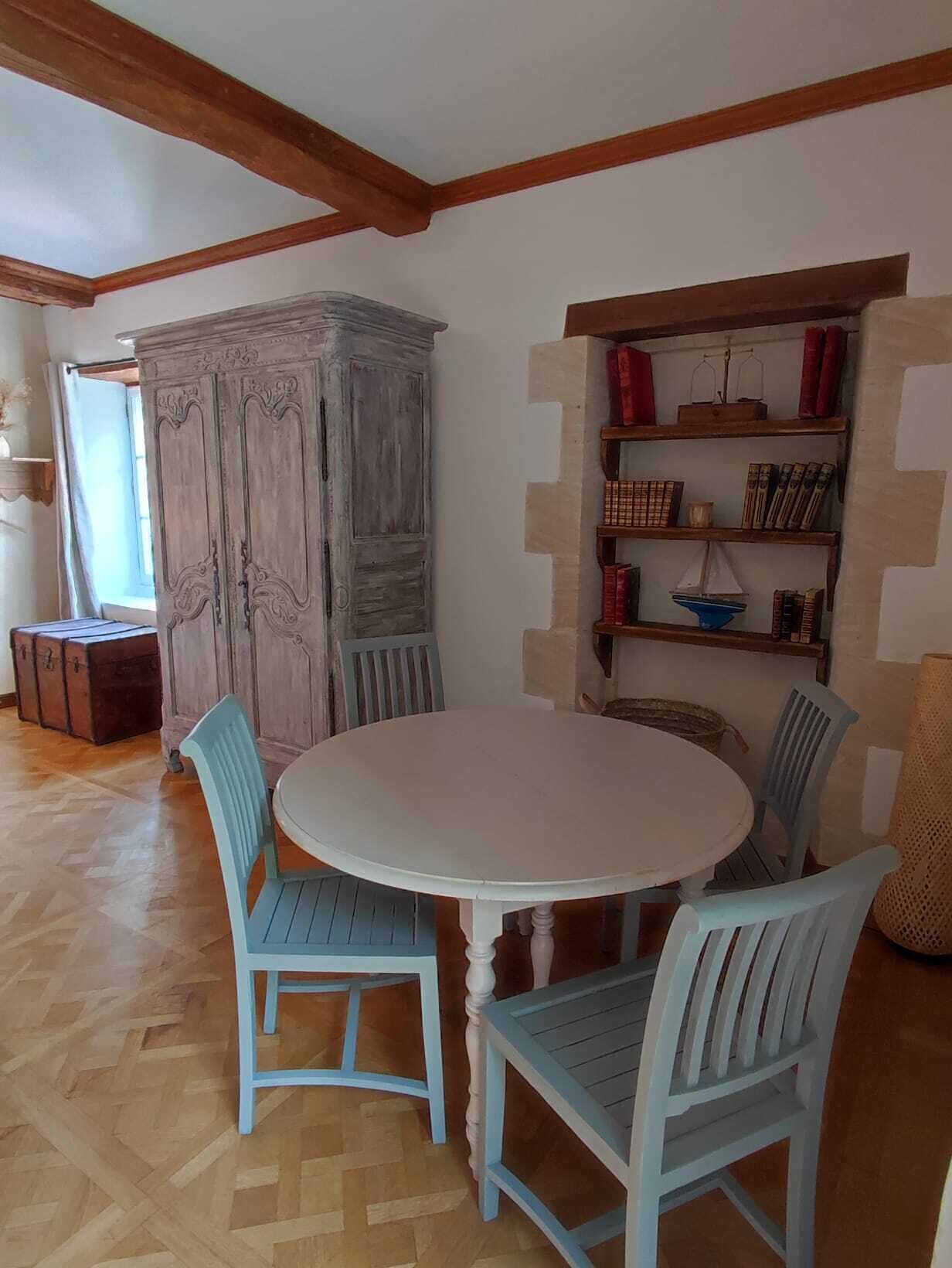 A dining area with a round table and four chairs, a wooden cabinet, and a bookshelf with books and decorative items.