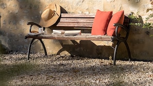 A wooden bench with a hat and books placed on it, set against a textured wall. - Chambre D'hôte à La Cour Souveraine Près des Plages du Débarquement et de Bayeux (Mosles)