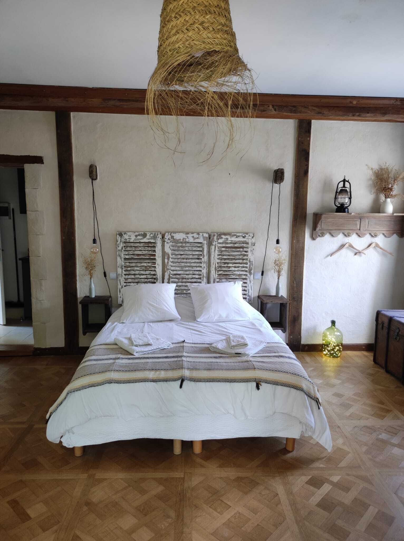 A bedroom with a large bed, wooden beams, a hanging light fixture, and a rustic decor style.