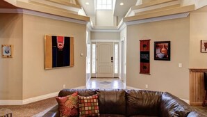 A spacious living room with a leather couch, a chandelier, and a door leading to another room.