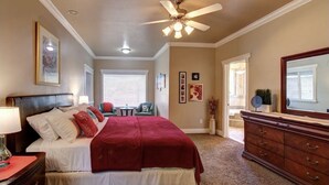 A bedroom with a bed, dresser, ceiling fan, and artwork on the walls.