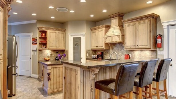 A kitchen with wooden cabinets, a marble countertop, and a bar area with stools.