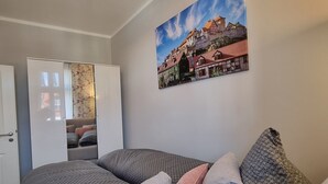Una habitación acogedora con una cama, un armario y un cuadro de un pueblo europeo.