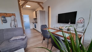 Un espacio habitable moderno con un sofá gris, mesa de comedor de madera y televisor montado en la pared.