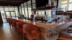 Una zona de bar con encimera de granito, varios taburetes y una variedad de botellas y vasos.