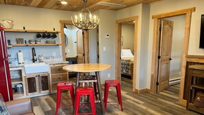 A cozy living room with a wooden dining table, red stools, and a patterned ottoman.